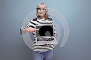 middle aged business woman demonstrates a laptop screen with a mockup for advertising on a bright studio background