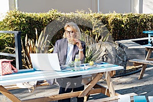 Middle-aged business woman having lunch at the park outdoor cafe, picnic area and working on laptop during her break