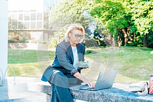 Middle-aged business woman having lunch sitting with laptop on bench at office park. Balanced diet lunch box for weight