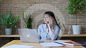 Middle-aged business woman sitting at desk with in office, talking on phone