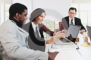 Middle aged business woman and young African businessman use laptop computer together, business people discuss at meeting table in