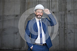 Middle aged businessman in hard hat and suit standing and smiling at work