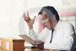 A middle-aged businessman holding a tablet is shocked by what happened to the screen