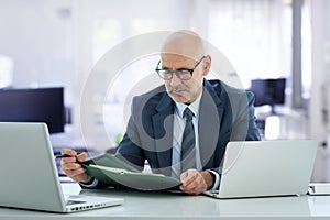 A middle-aged businessman sitting at his desk in the office and using a laptop for work