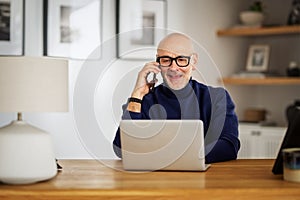 Middle aged businessman using smartphone and laptop while working from home