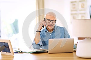 Middle aged businessman using smartphone and laptop while working from home