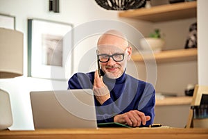 Middle aged businessman using smartphone and laptop while working from home