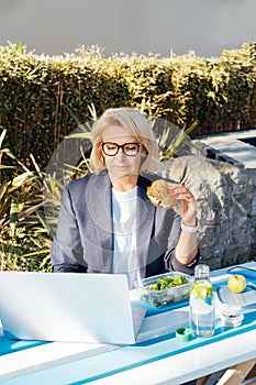 Middle-aged businesswoman having lunch at the park outdoor cafe, picnic area and working on laptop during her break