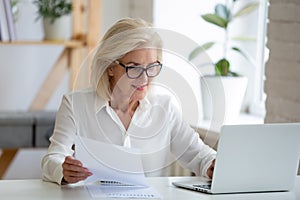 Middle-aged businesswoman typing on pc holds paper prepares report