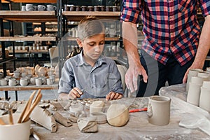 Middle aged caucasian man teaches his little brother to work with clay on pottery workshop. Art work concept.