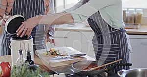 Middle aged caucasian woman putting food waste in bin in kitchen at home, slow motion