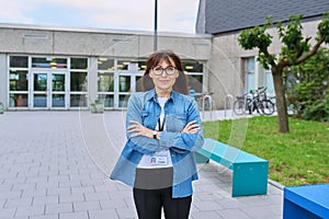 Middle aged confident woman teacher with crossed arms near school building