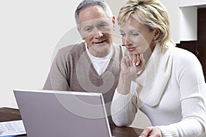 Middle-aged couple counting bills using laptop in kitchen