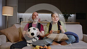 Middle aged couple of football fans watching soccer game on tv at home