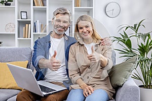 Middle-aged couple giving thumbs up in a cozy living room