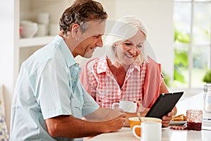 Middle Aged Couple Looking At Digital Tablet Over Breakfast