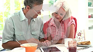 Middle Aged Couple Looking At Digital Tablet Over Breakfast