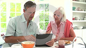 Middle Aged Couple Looking At Digital Tablet Over Breakfast