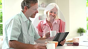 Middle Aged Couple Looking At Digital Tablet Over Breakfast