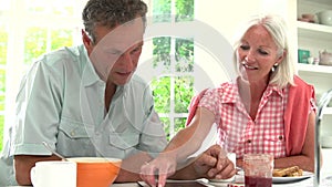 Middle Aged Couple Looking At Digital Tablet Over Breakfast