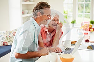 Middle Aged Couple Looking At Laptop Over Breakfast