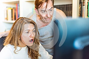 Middle-aged couple looking surprised at computer at home