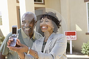 Middle-aged couple photographing in front of new home