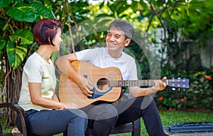 Middle aged  couple playing guitar while relax sitting on bench