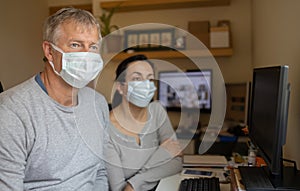 Middle aged couple with protective mask working at home due to coronavirus quarantine