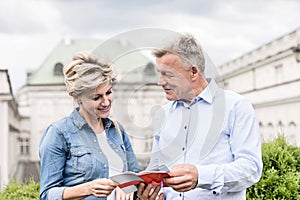 Middle-aged couple reading guidebook outside building