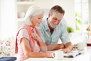 Middle Aged Couple Reading Magazine Over Breakfast