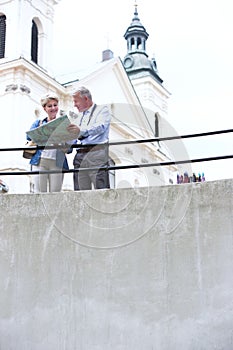 Middle-aged couple reading map by railing outside church