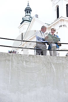 Middle-aged couple reading map by railing outside church
