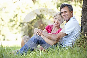 Middle Aged Couple Relaxing In Countryside Leaning Against Tree