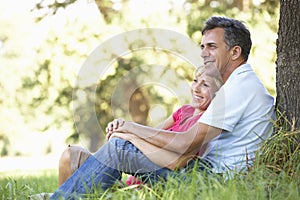 Middle Aged Couple Relaxing In Countryside Leaning Against Tree