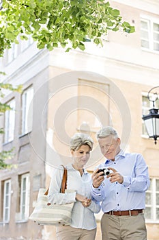 Middle-aged couple reviewing photos on digital camera outside building