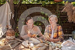 Middle-aged couple sitting at table, shucking corn