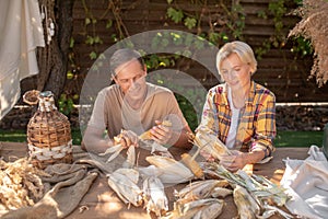 Middle-aged couple sitting at table, shucking corn in the garden