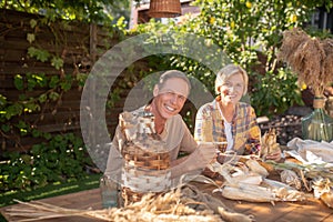 Middle-aged couple sitting at wooden table, shucking corn outside