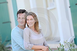 Middle-aged couple standing and smiling in front of house