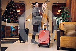 middle aged couple standing with suitcases and smiling at camera in hotel hallway