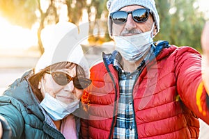 Middle aged couple taking a selfie wearing surgical masks - seniors on vacation enjoy the freedom after the end of the lockdown -