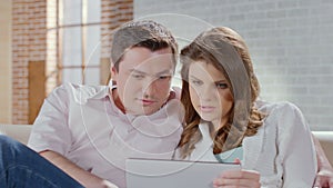 Middle-aged couple talking, laughing, viewing photos on tablet