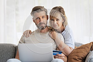 Middle-aged couple wearing casual clothes and sitting at home on the sofa and shopping online