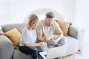 Middle-aged couple wearing casual clothes and sitting at home on the sofa and using a laptop