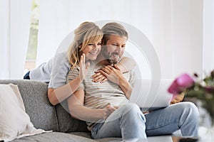 Middle-aged couple wearing casual clothes and sitting at home on the sofa and using a laptop