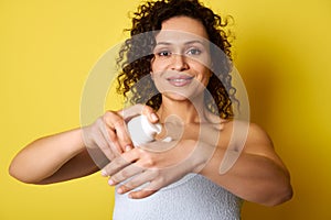 A middle-aged curly woman squeezing moisturizing cream from a bottle and applying it on hands. Body care concepts