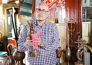 Middle aged man owner of antiques shop wiping vintage goods