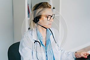 Middle aged doctor in white coat and video conferencing headset make online video call consult patient on laptop