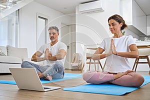 Middle aged family couple doing yoga at home looking at laptop.